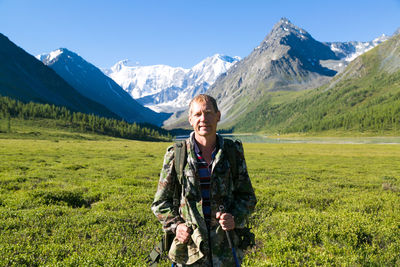 Portrait of man with backpack standing on green field against mountains