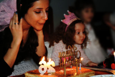 Woman with daughter blowing candles in darkroom