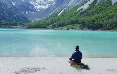 Rear view of man sitting on rock by lake