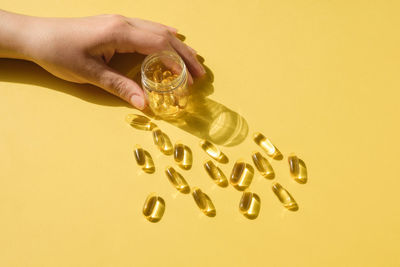 Woman's hand holding glass pill bottle. big golden tablets. omega 3 capsules. close up, top view.