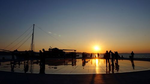 Silhouette people by sea against clear sky during sunset