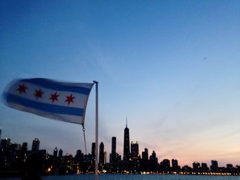 Flag of chicago waving by river against city during sunset