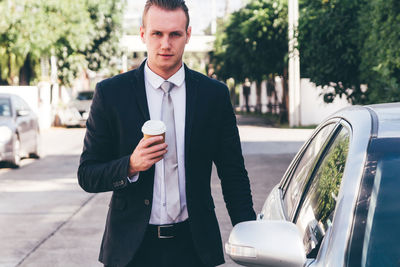 Portrait of businessman standing with car on road