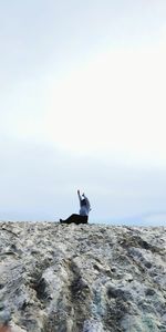 Man sitting on rock by sea against sky