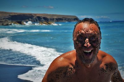 Portrait of cheerful man with mud on face standing at beach