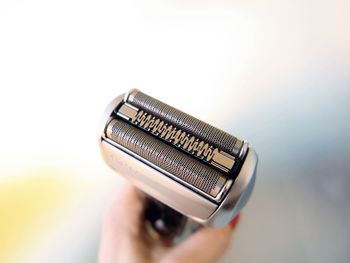 Close-up of hand using shaving equipment  against white background