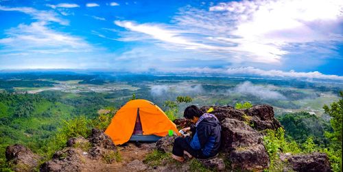 Man using mobile phone by tent on landscape against sky