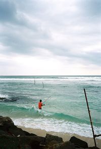 Man fishing in sea against sky