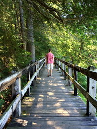 Rear view of man walking on wooden footbridge