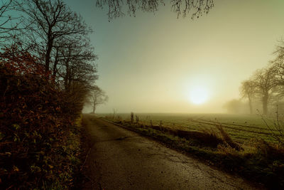 Dirt road amidst field against sky during sunset