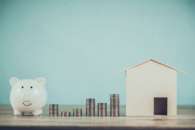 Close-up of model home with coins and piggy bank on table against blue background