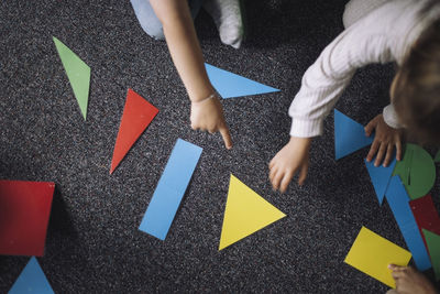 Directly above view of kids playing with geometric shapes on floor in classroom at kindergarten