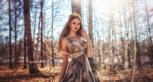 Portrait of beautiful young woman standing against trees at forest