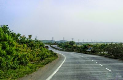 Empty road by trees against sky