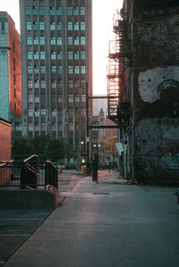 Empty road amidst buildings against sky in city