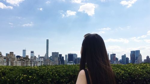 Rear view of woman with skyscrapers against cloudy sky