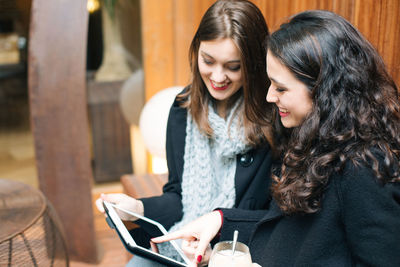 Young woman using smart phone while sitting on laptop