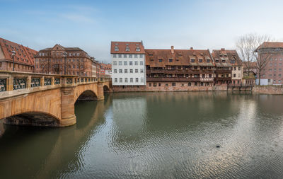 Bridge over river by buildings against sky