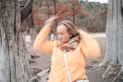 Woman standing by tree trunk in forest