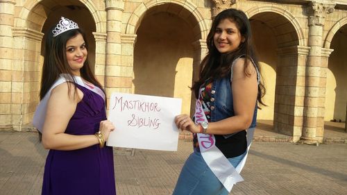 Portrait of smiling females showing placard while standing against building