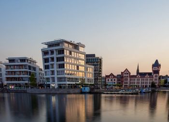 Buildings by river against clear sky