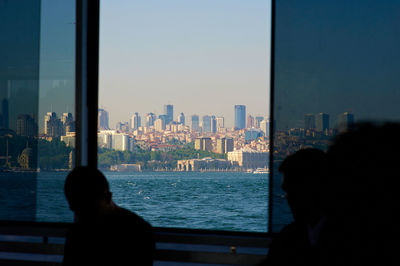 City buildings by sea against clear sky seen through window