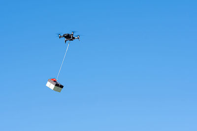 Multicopter drone flying with a gift box isolated on a blue sky, concept of modern fast delivery