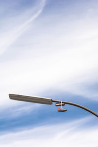 Low angle view of shoes hanging on street light against cloudy sky