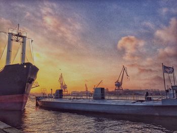 Cranes at harbor against sky during sunset