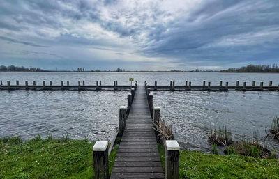 Pier over lake against cloudy sky