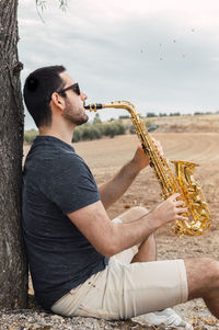 Side view of young man playing guitar against sky