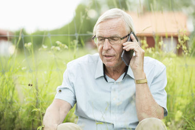 Senior man using mobile phone while sitting in yard