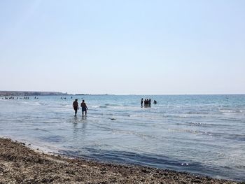 People standing on beach against clear sky