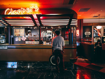 Rear view of man standing at illuminated restaurant