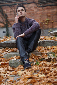 Full length of young man sitting on autumn leaves