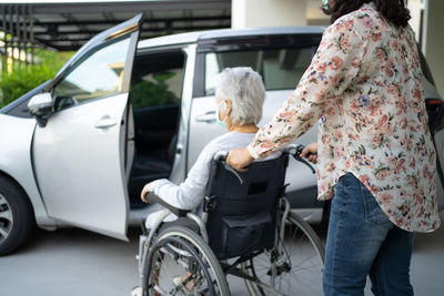 Help and support asian senior old lady woman patient sitting on wheelchair prepare get to her car 