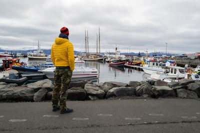 Man in a yellow jacket standing overlooking husavik harbour with boats