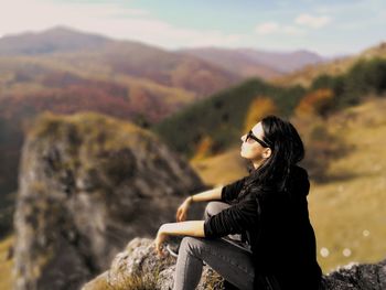 Young woman sitting on cliff against mountains