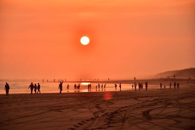 Silhouette people on beach against orange sky