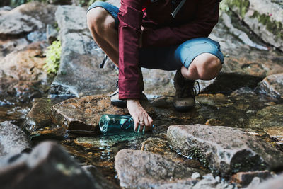 Hiker crouching on rocks, filling bottle up with cold mountain water. enjoying the outdoors