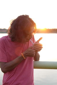 Man lighting cigarette while standing by sea during sunset