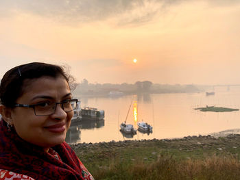 Portrait of smiling woman against lake during sunset