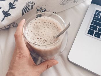 Cropped image of hand holding drink by laptop on bed