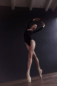 A ballerina in a bodysuit and pointe shoes moves around the room with long strides