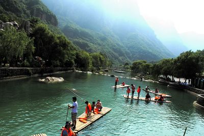 People on wooden raft in river against mountains