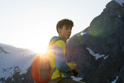 Side view portrait of boy wearing backpack against mountain during winter