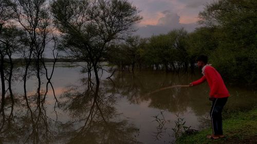 Side view of man standing by lake against sky