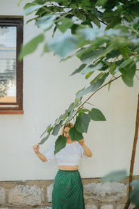 Woman standing by plants against wall
