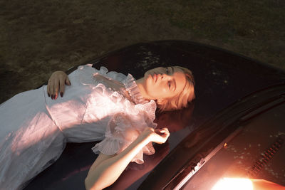 A woman in a dress lying on the hood of a car in the evening