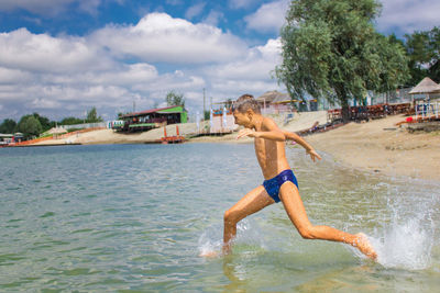 Boy running at beach against sky